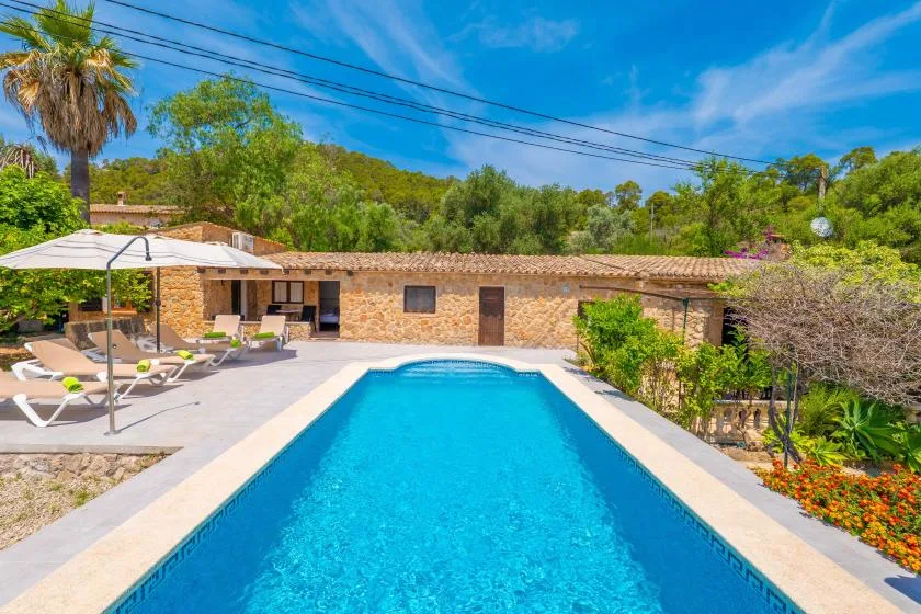 A swimming pool beside a stone building, with lounge seating on the patio.