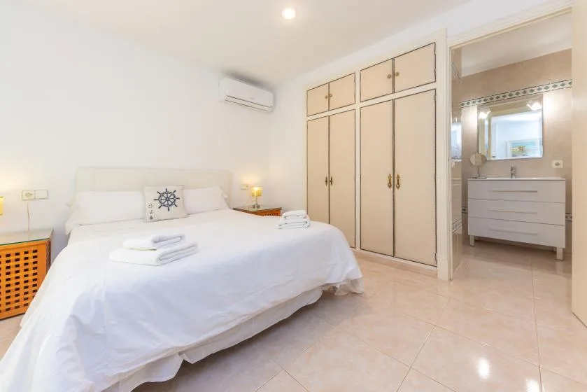 A bright bedroom with a white bed and an open bathroom area.