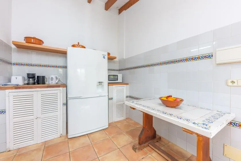 A tiled kitchen with a refrigerator, countertop, and wooden dining table.