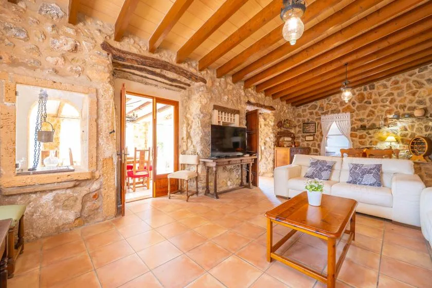 A stone-walled living room with exposed wooden ceiling beams and a white sofa.