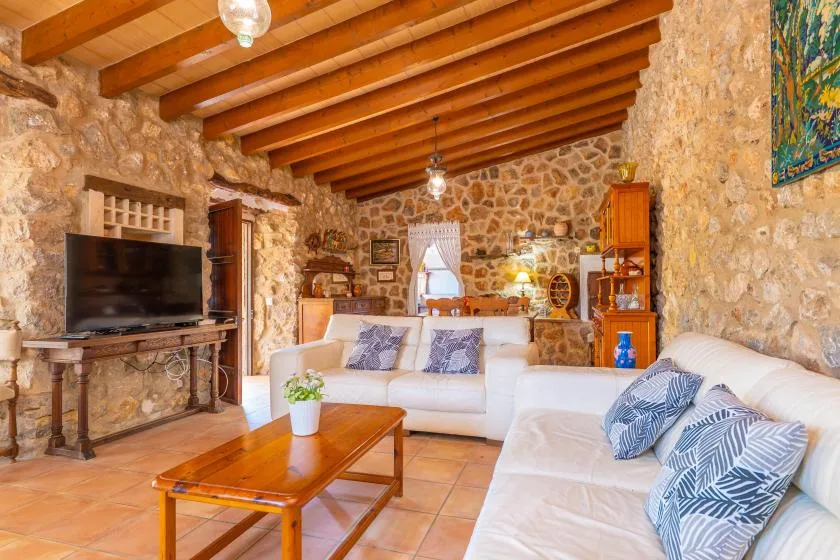 A living room with stone walls, exposed wooden beams, and light-colored seating.