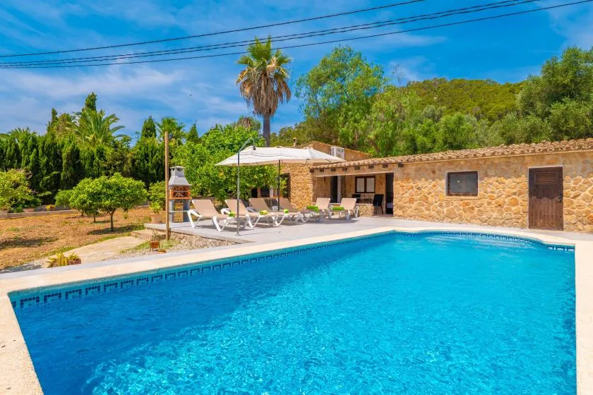 An outdoor swimming pool sits beside a stone building and shaded seating area.