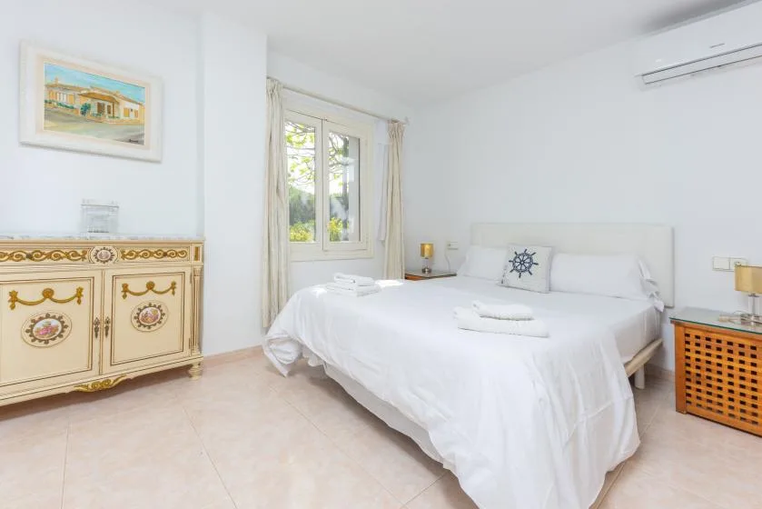 A bright bedroom with a white bed and a window beside it.