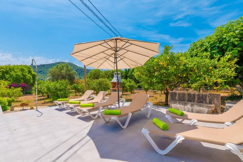 A sunny outdoor patio with lounge seating beneath a large umbrella.