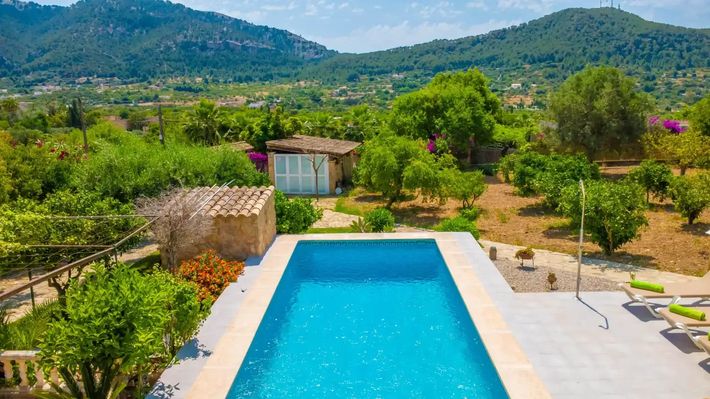An outdoor swimming pool sits among gardens with green hills in the background.