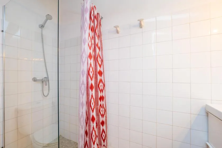 A tiled bathroom shower with a red-and-white patterned curtain.