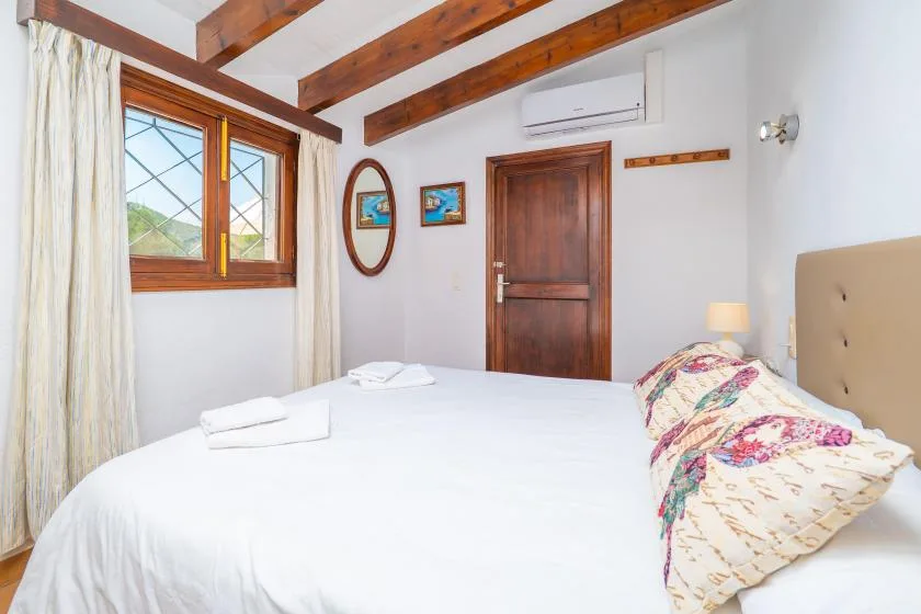 A bedroom with a large bed, wooden ceiling beams, and a window with curtains.