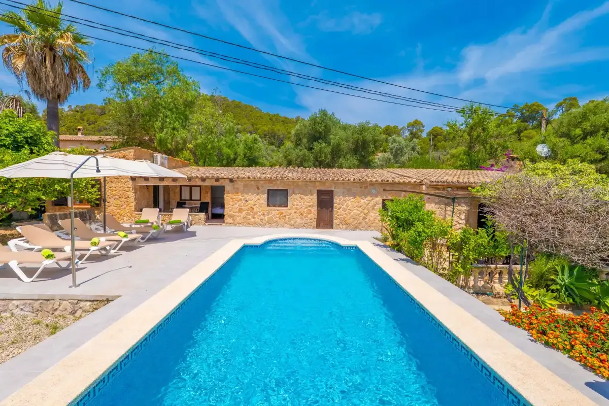 A swimming pool sits in front of a low stone building, with loungers nearby.