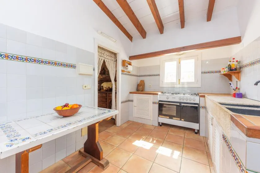 A tiled kitchen with a stove, sink, and wooden ceiling beams.