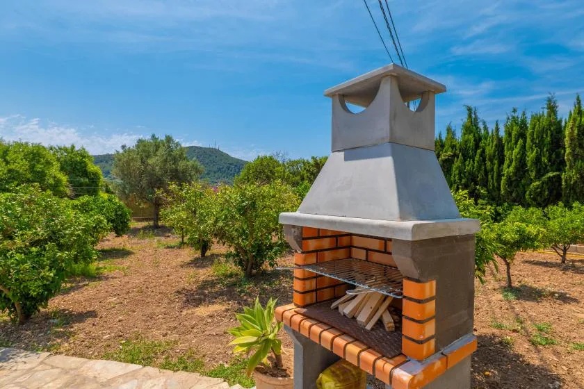 An outdoor brick barbecue stands among trees beneath a clear blue sky.