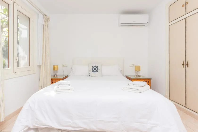 A bright bedroom with a neatly made bed and windows along one wall.