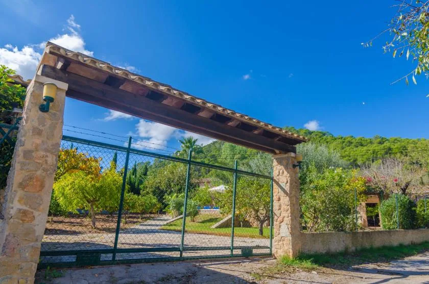 A stone entrance arch frames a green metal gate beside a landscaped outdoor area.