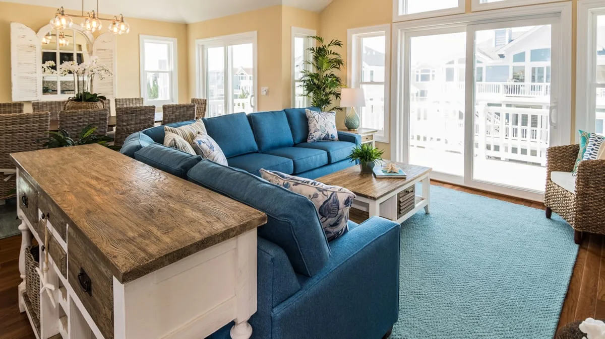 Una sala luminosa con asientos azules, una isla de cocina y ventanas grandes.