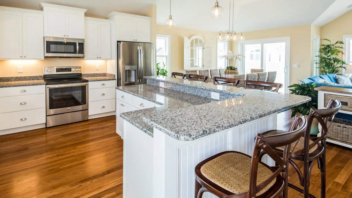 Una cocina luminosa cuenta con gabinetes blancos, electrodomésticos de acero inoxidable y una gran isla con cubierta de piedra.