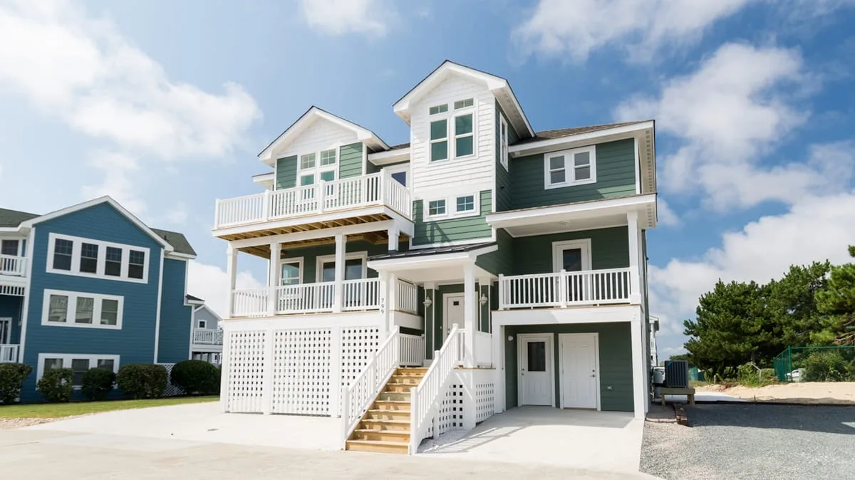 Una casa grande de estilo costero con balcones blancos y escaleras exteriores.