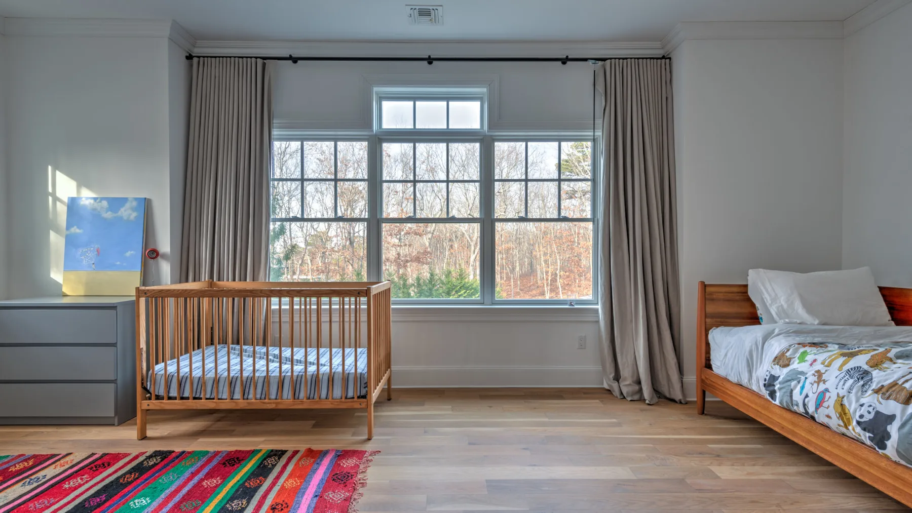 Un dormitorio con una cuna de madera, una cama y una ventana grande.