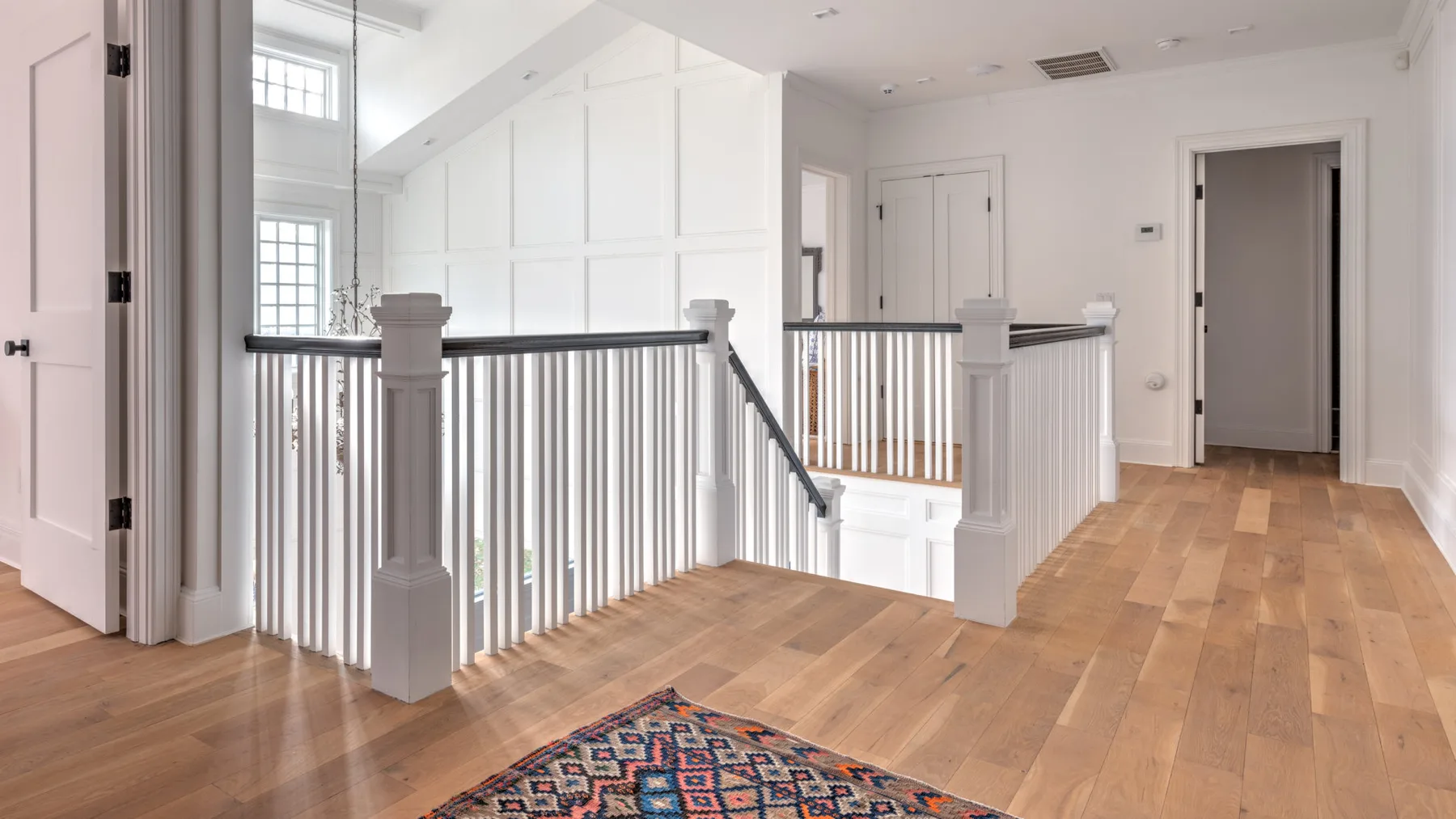 Un rellano luminoso con suelo de madera y una barandilla blanca alrededor de la escalera.