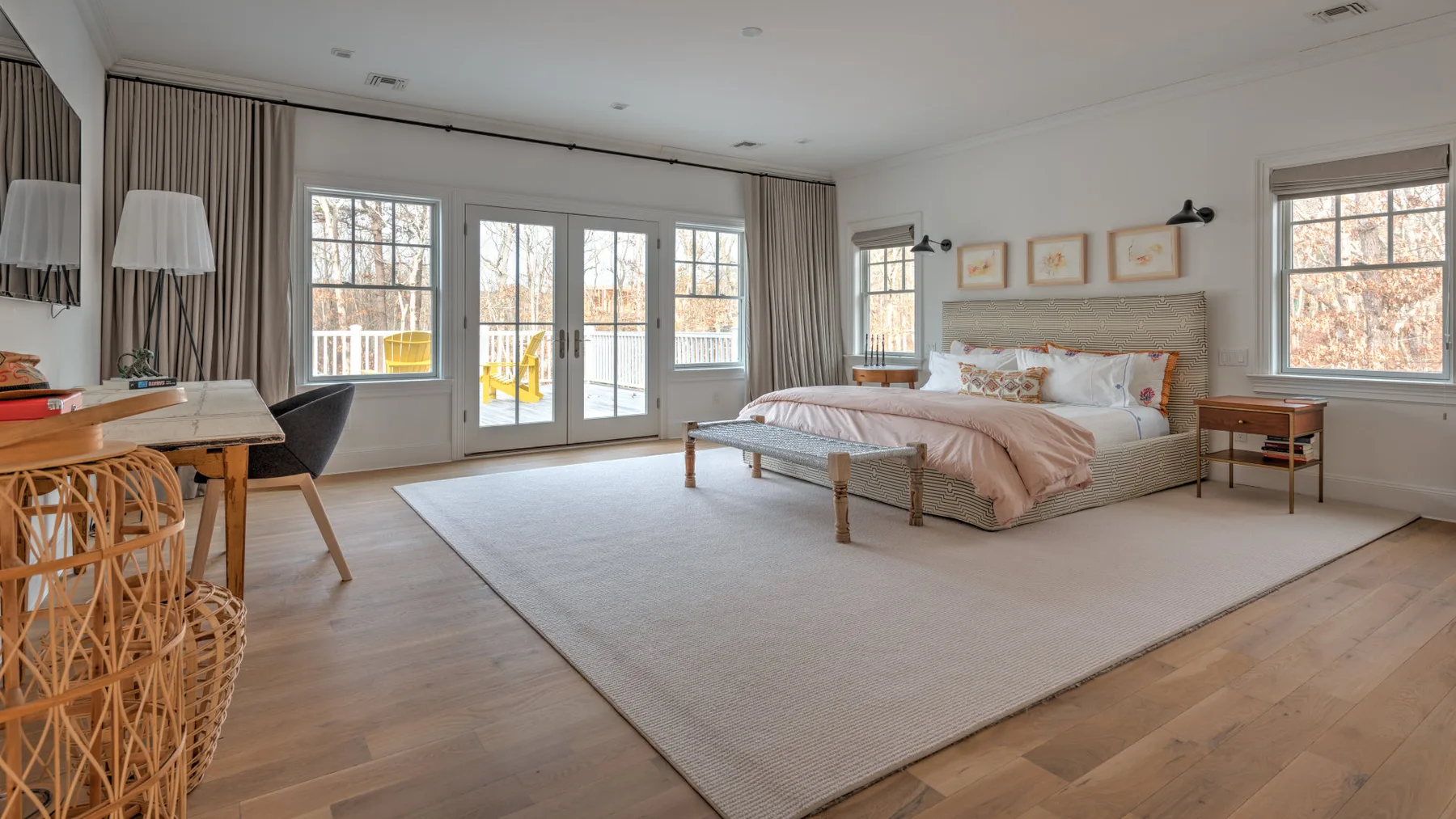 Un dormitorio luminoso con una cama grande, una alfombra clara y varias ventanas.