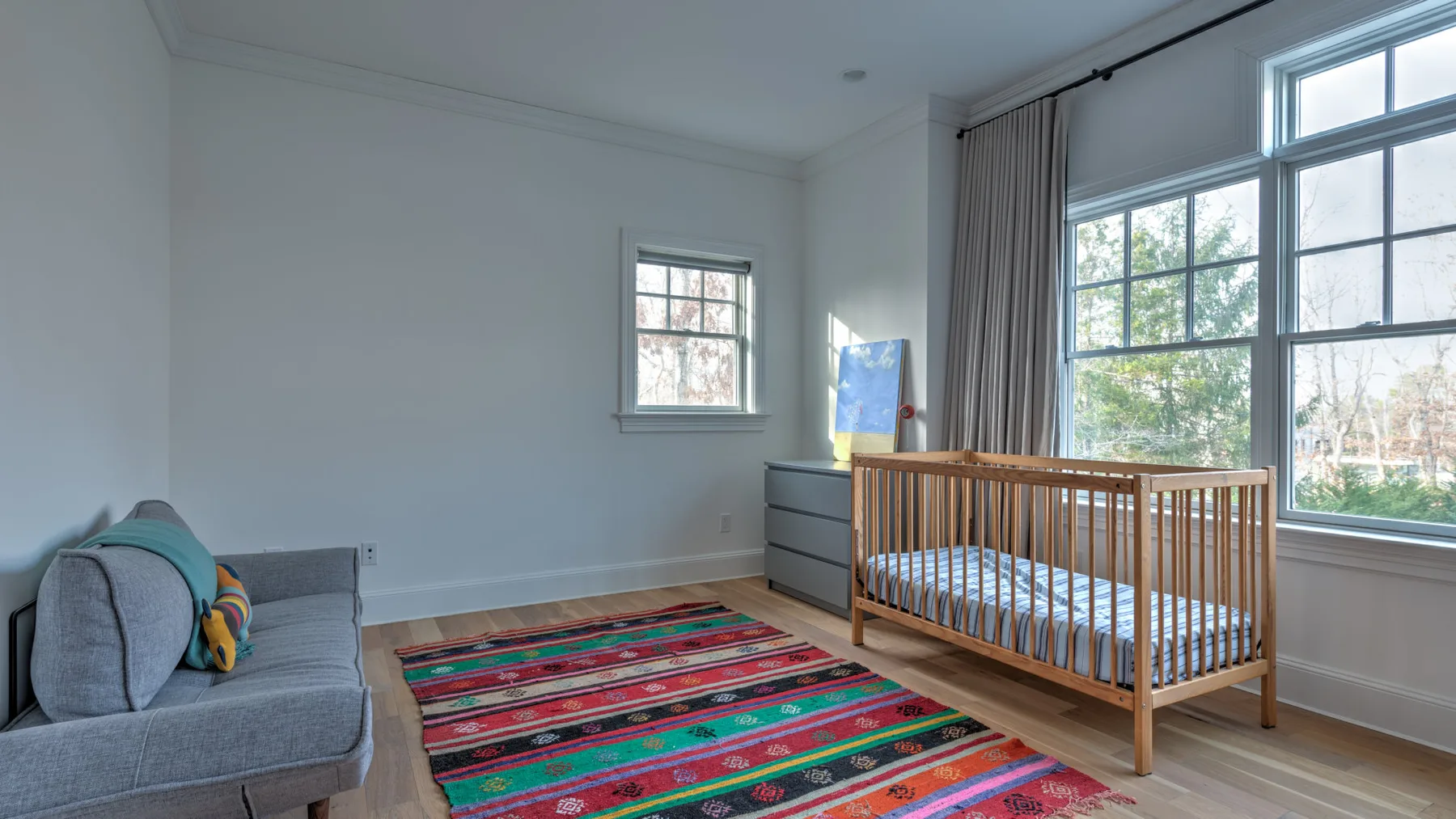 Un dormitorio infantil luminoso con una cuna de madera junto a grandes ventanas.