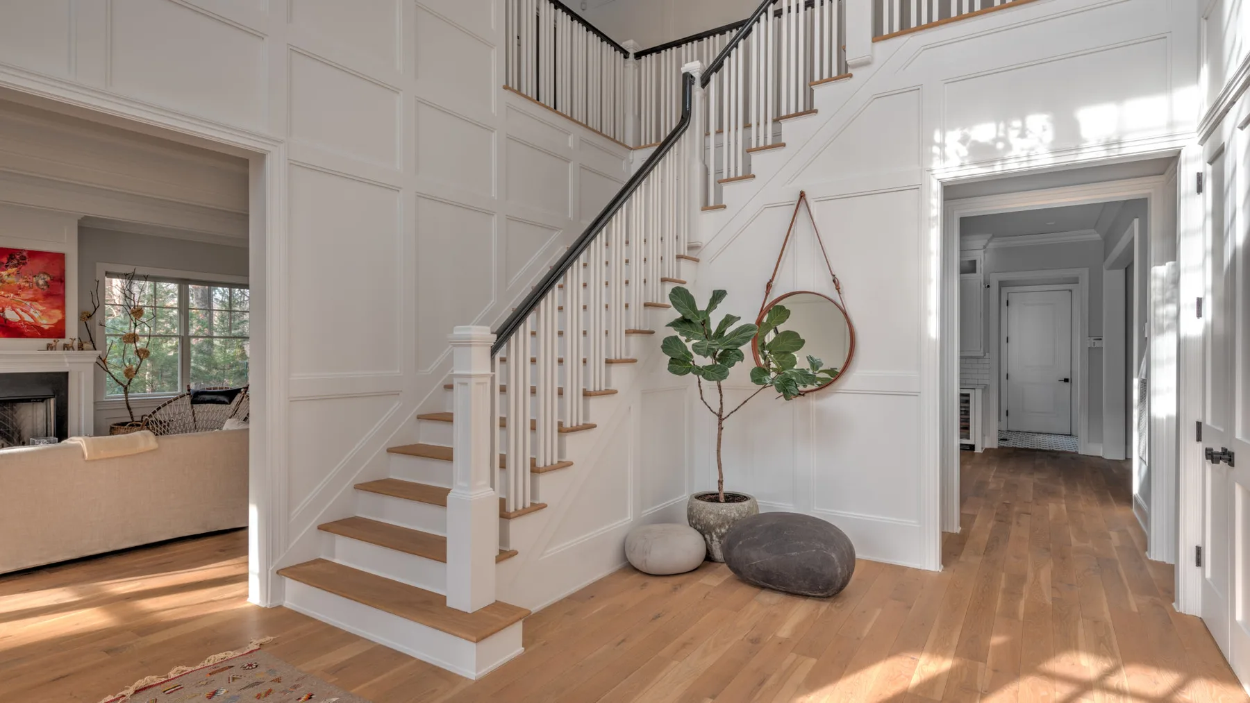 Un recibidor luminoso con una escalera, suelo de madera y plantas en macetas.