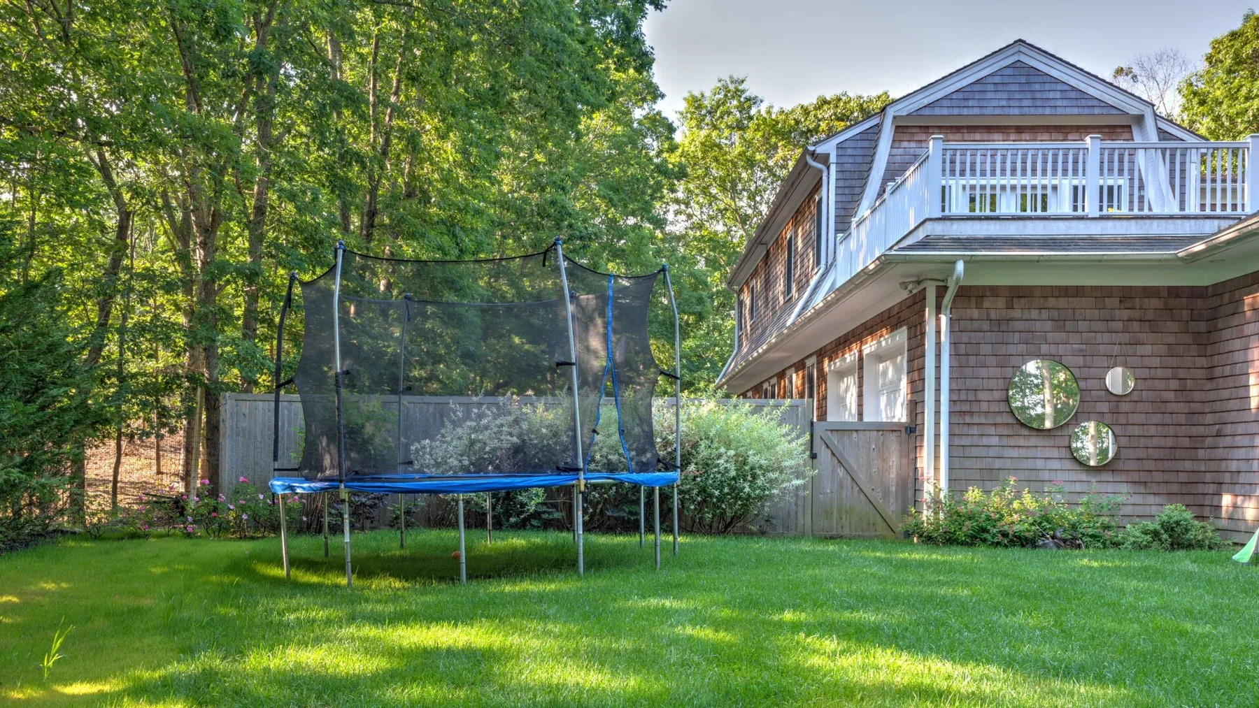 Una casa y un trampolín están junto a un césped verde rodeado de árboles.
