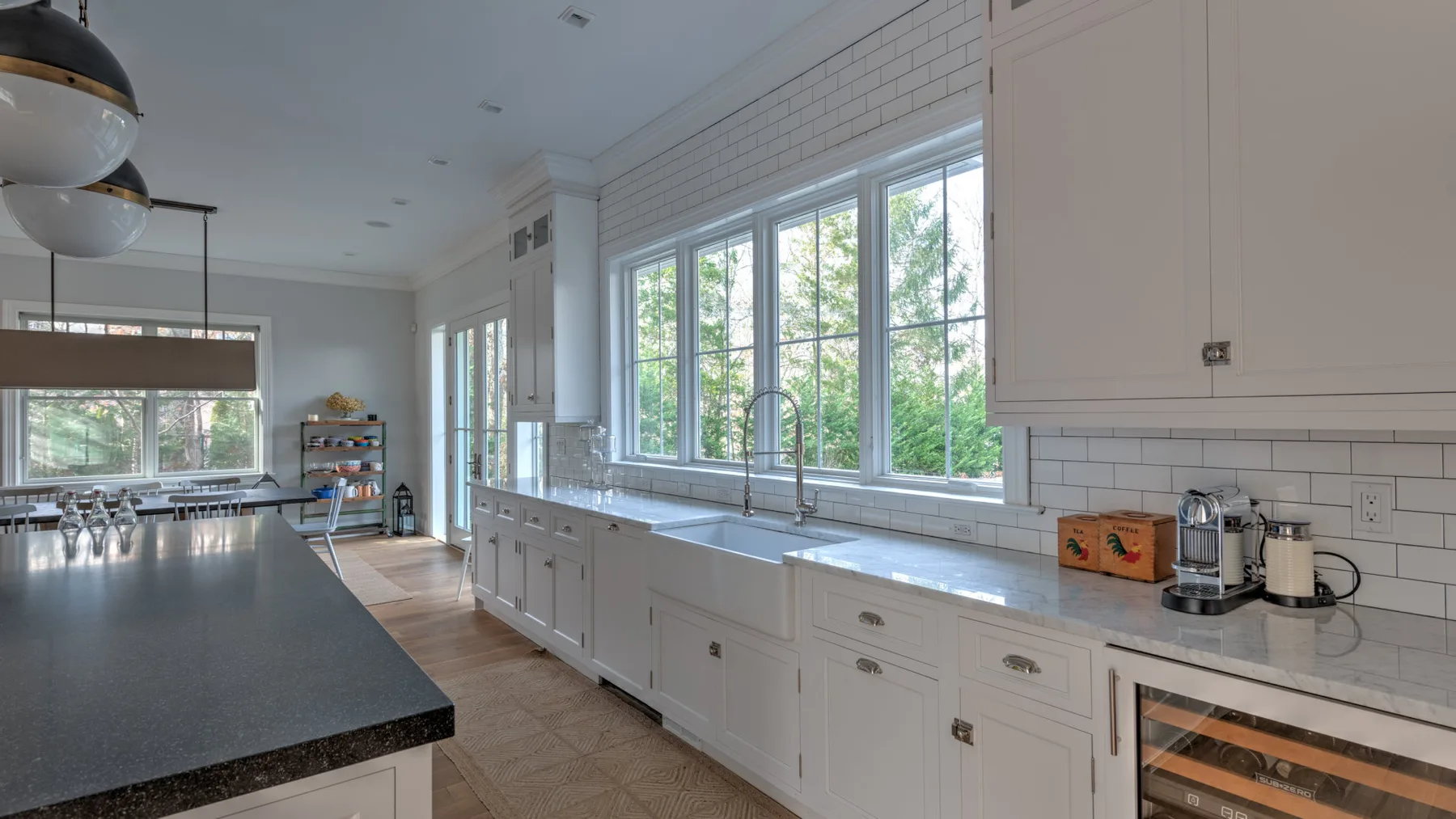 Una cocina luminosa con gabinetes blancos, una encimera larga y ventanas grandes.