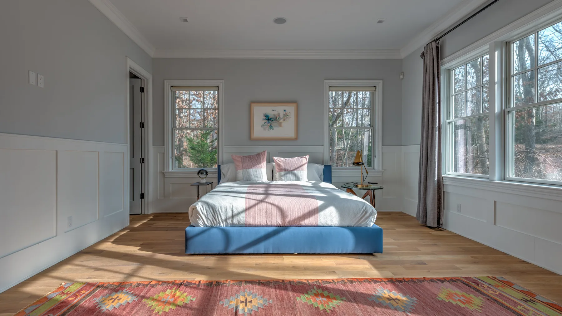 Un dormitorio con una cama bajo un cuadro enmarcado y grandes ventanas.