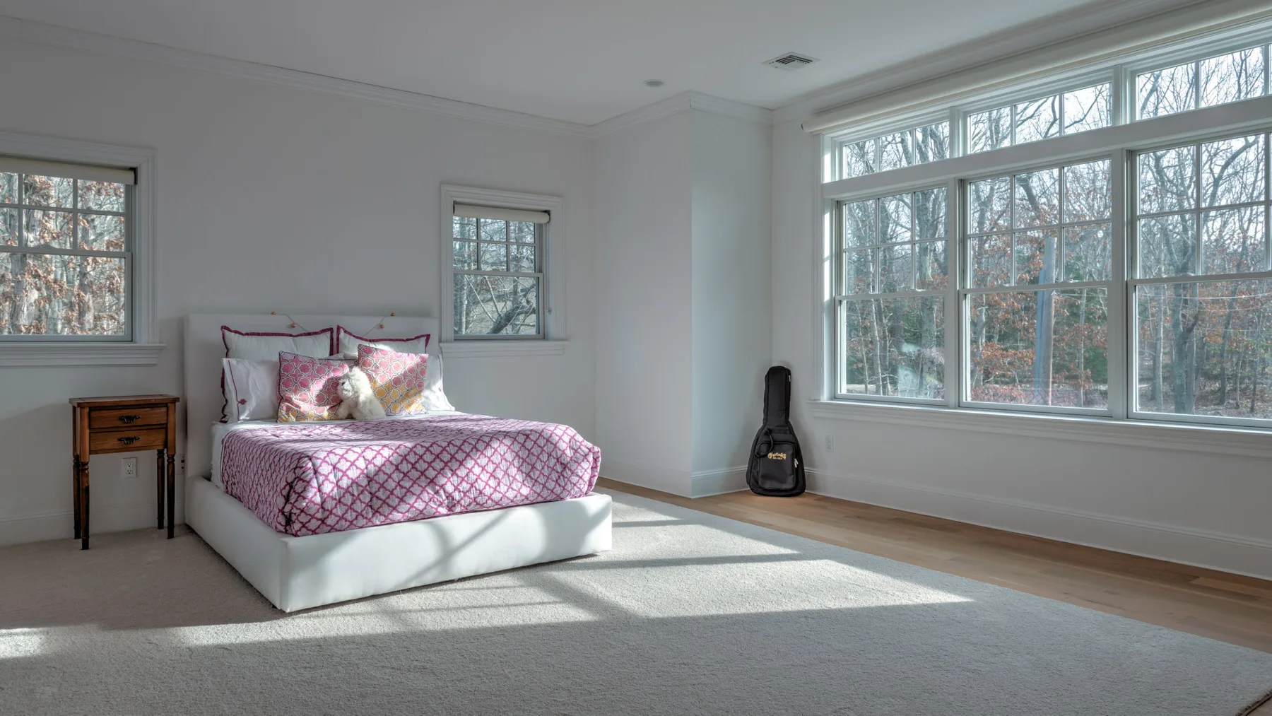 Un dormitorio luminoso con una cama junto a grandes ventanas con vista a los árboles.
