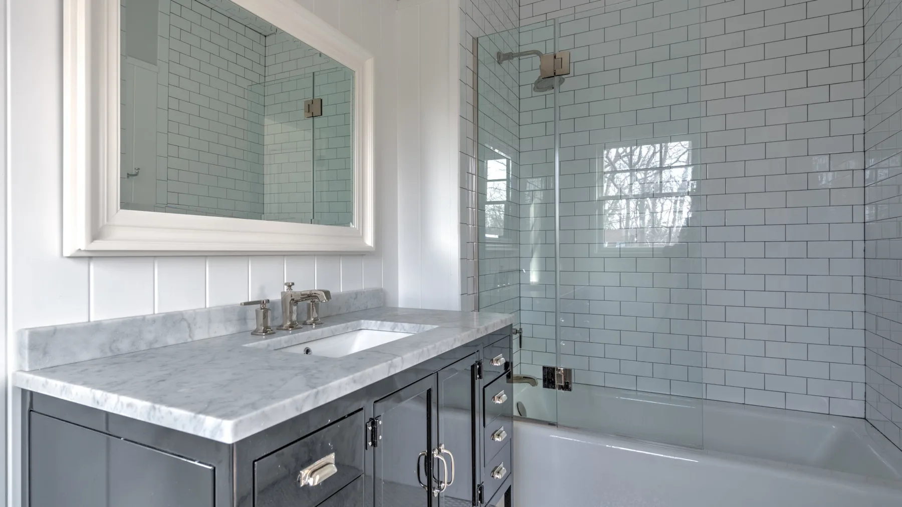Un tocador de baño con un espejo grande junto a una bañera con ducha y azulejos.