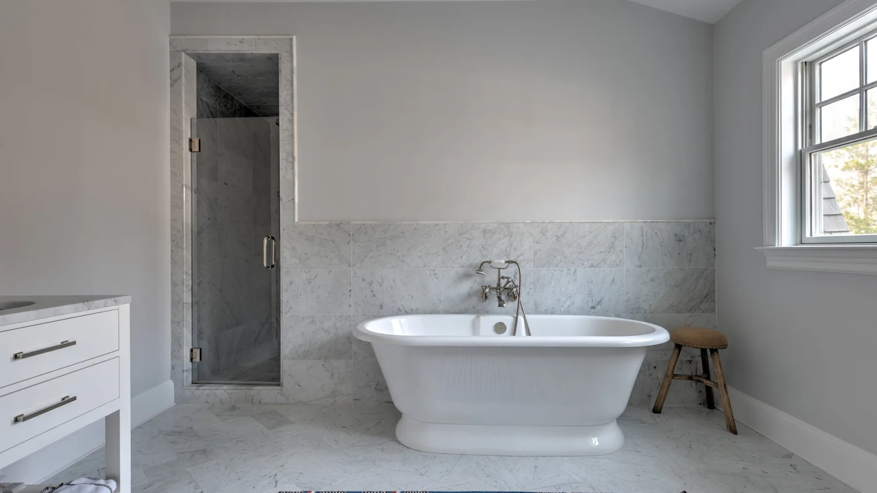 Un baño con bañera exenta, paredes de mármol y una ventana.