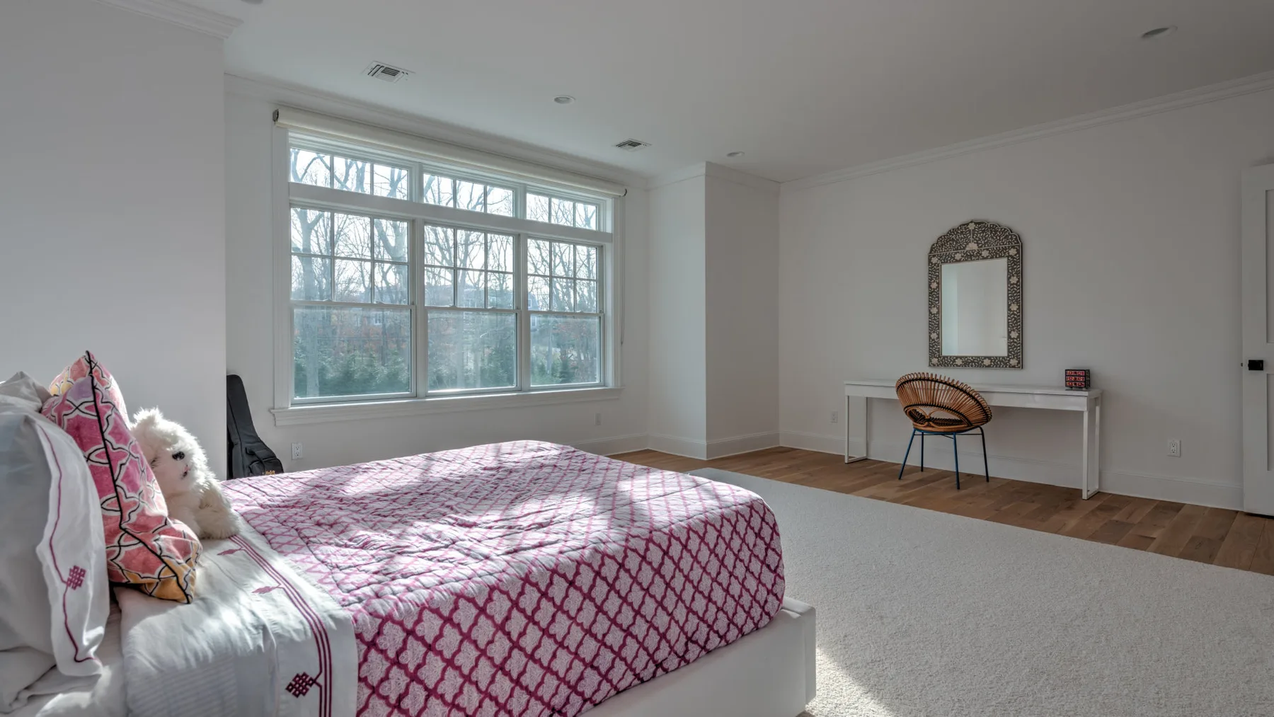 Un dormitorio luminoso con una cama junto a una ventana grande y un tocador.