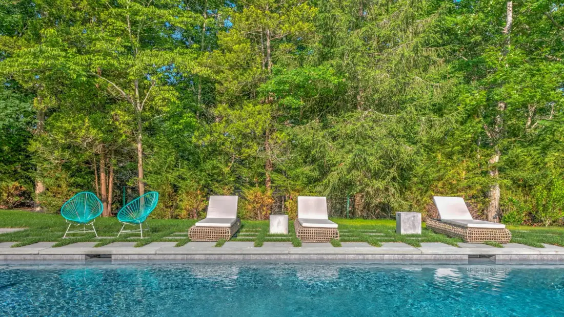 Una piscina al aire libre con tumbonas y árboles frondosos detrás.