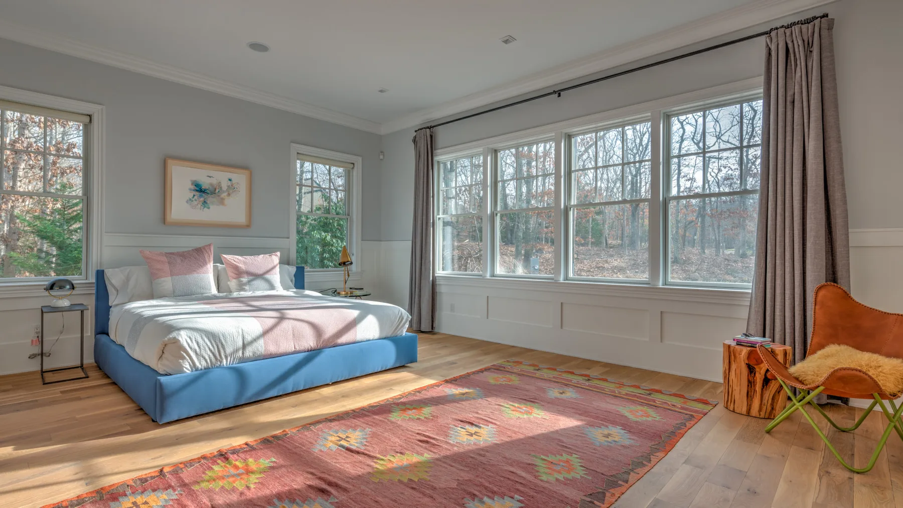 Un dormitorio luminoso tiene una cama junto a grandes ventanas y una alfombra estampada.