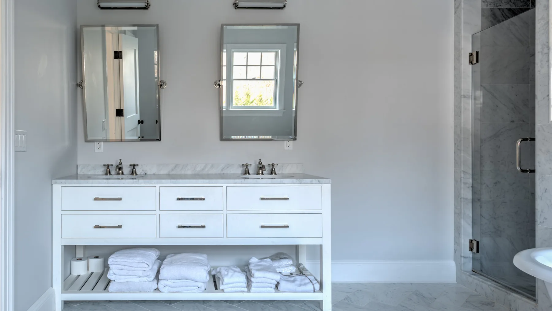 Un baño luminoso cuenta con un tocador doble, espejos y un estante abierto con toallas dobladas.