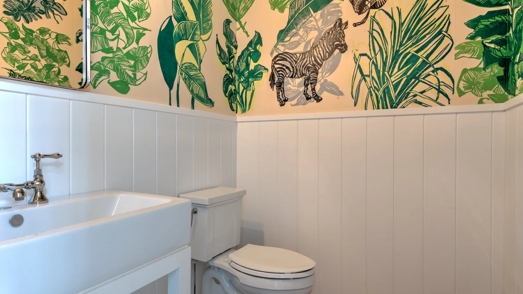 Un baño con bañera e inodoro bajo un papel tapiz botánico.