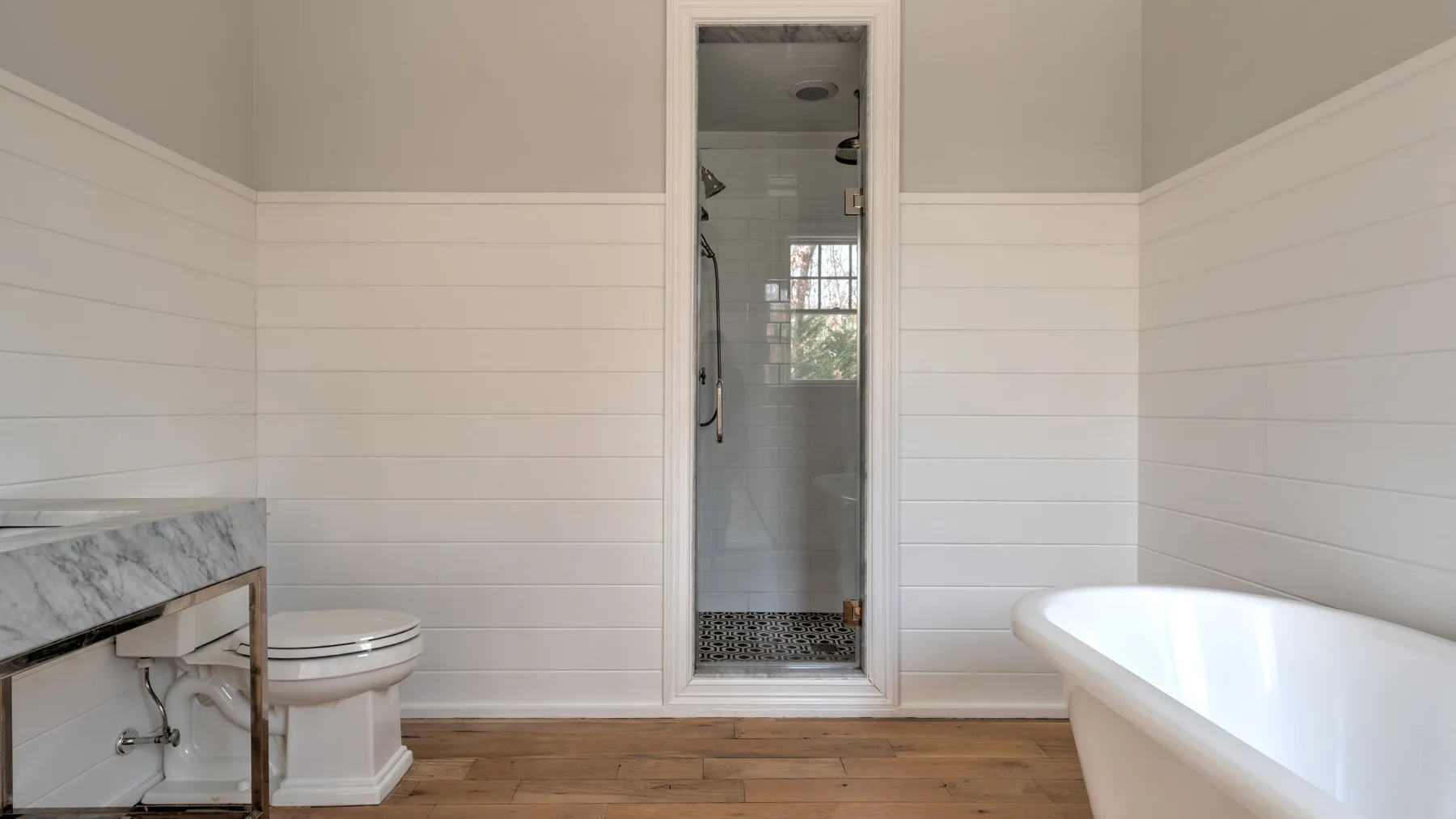 Un baño con una bañera exenta, paredes revestidas y una puerta hacia la ducha.