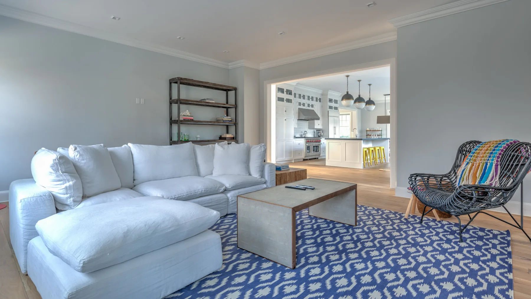 Una sala luminosa con un sofá seccional blanco y una alfombra azul estampada.