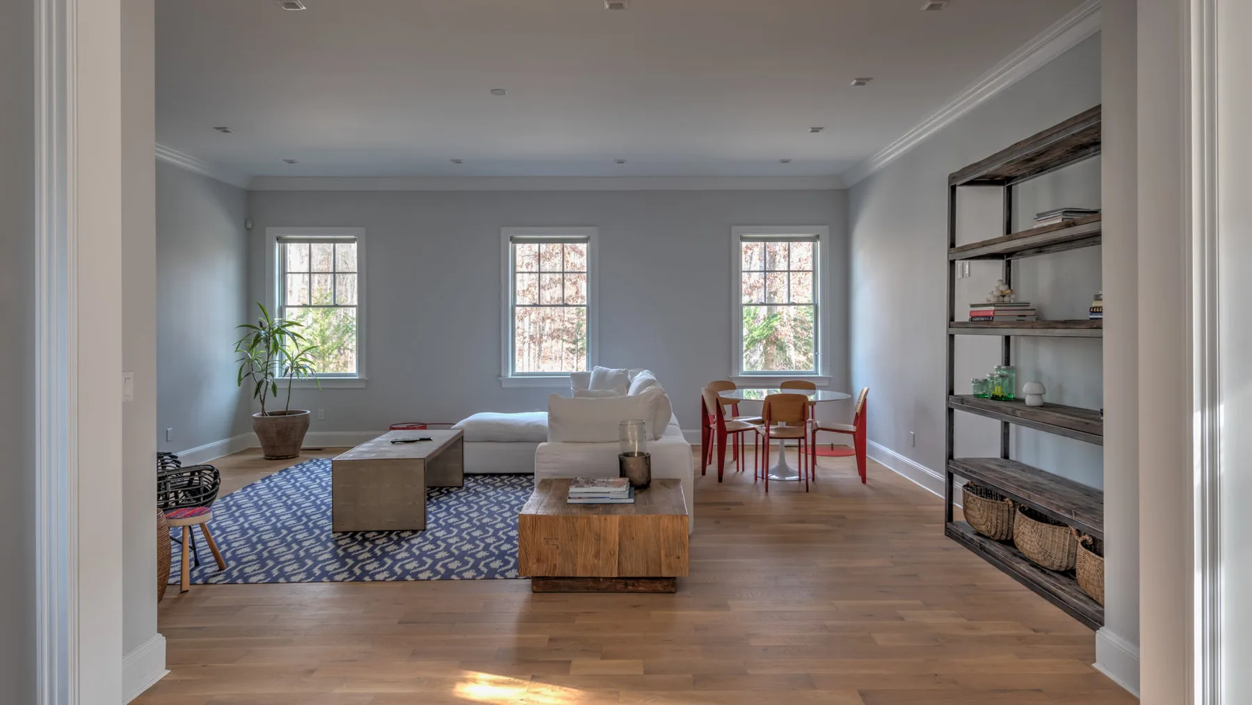 Una sala de estar con asientos, una alfombra y una mesa de comedor junto a las ventanas.
