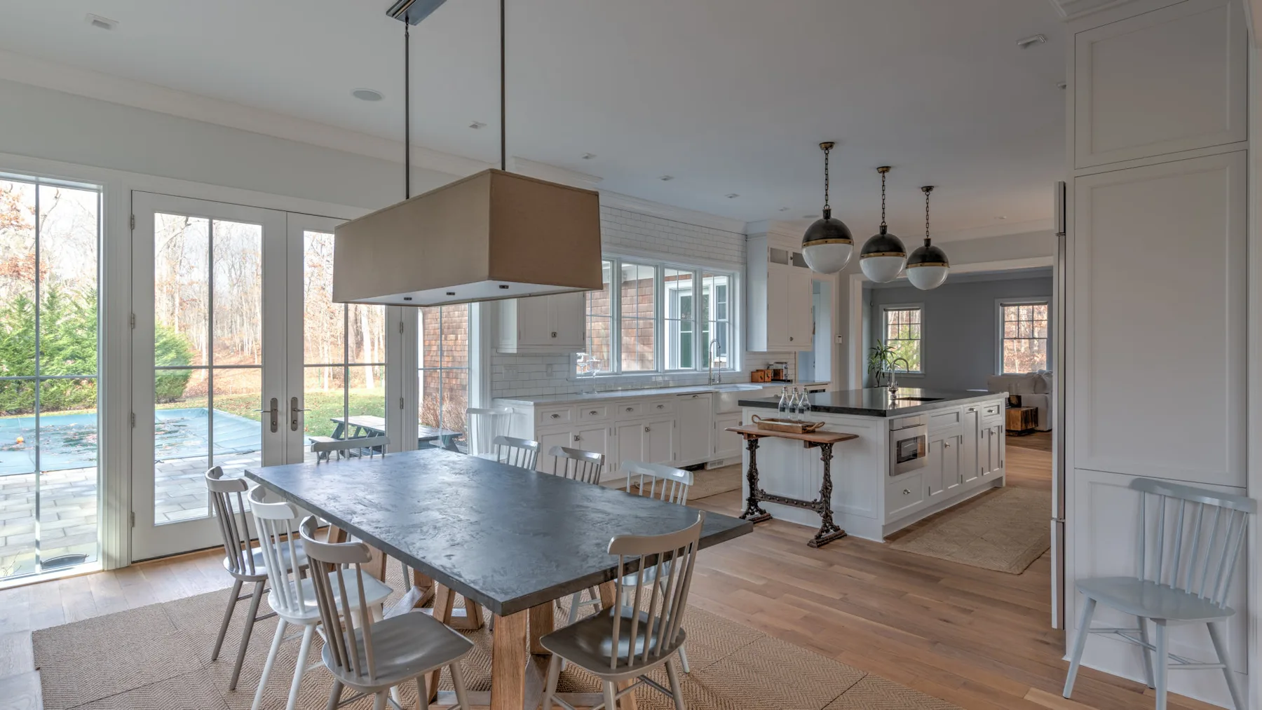 Una luminosa cocina y comedor con una mesa larga junto a grandes ventanas y puertas de vidrio.