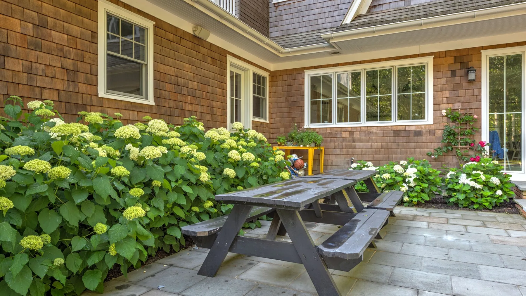 Un patio exterior con una mesa de picnic junto a una casa con revestimiento de tejas.