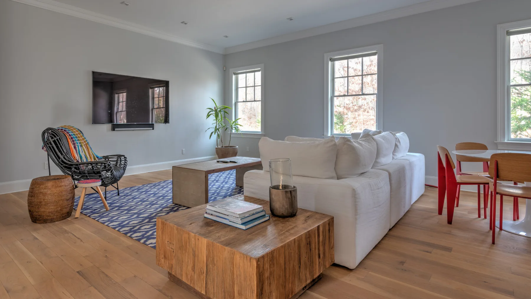 Una sala de estar luminosa con asientos claros, mesas de madera y ventanas grandes.