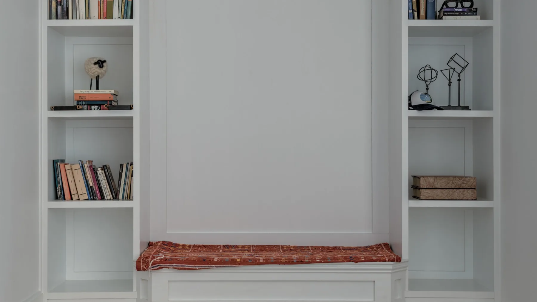 Un asiento empotrado con un cojín rojo estampado se encuentra entre dos librerías blancas.