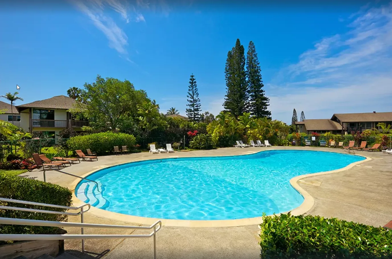 An outdoor swimming pool is surrounded by deck space, lounge seating, and greenery.