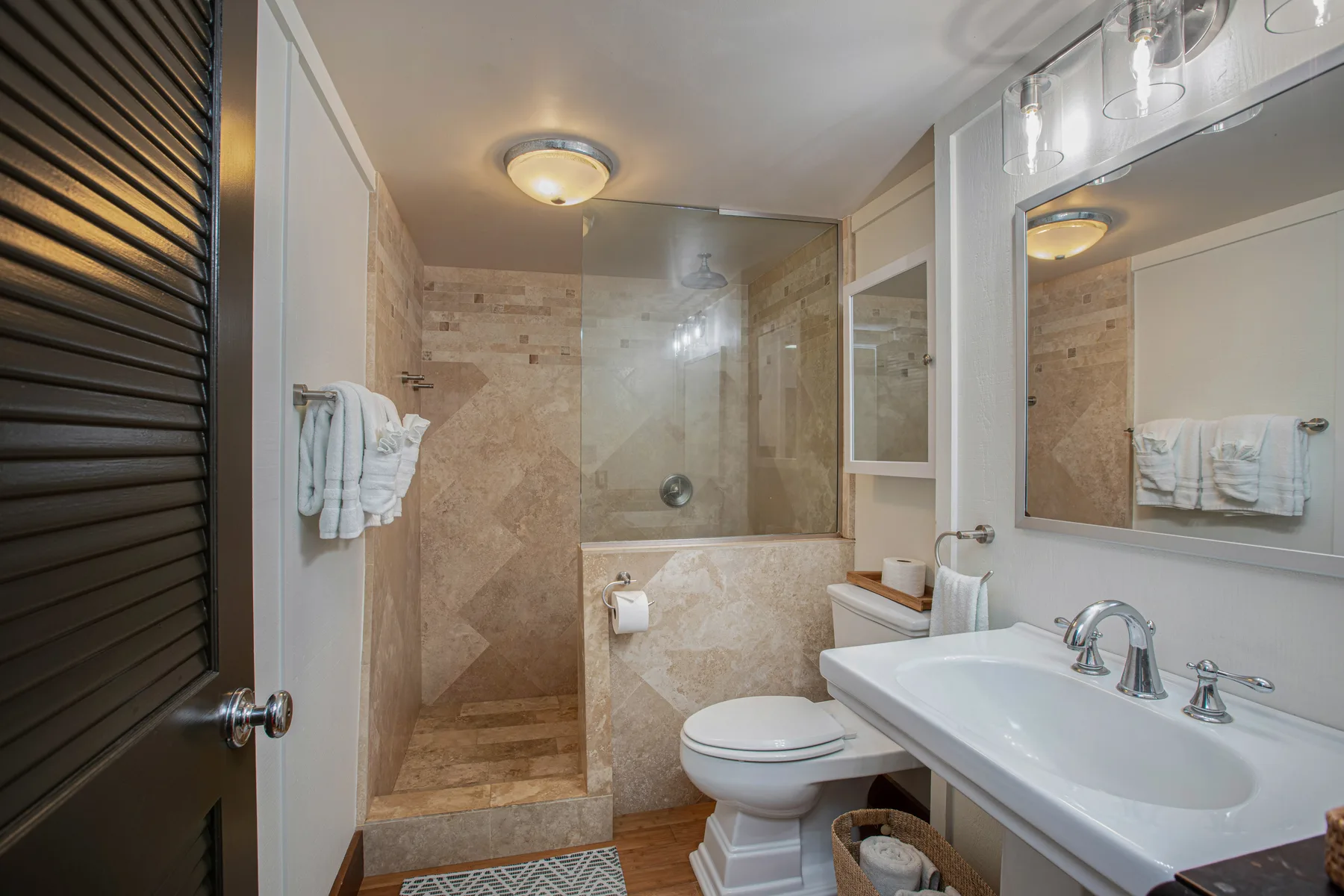 A bathroom with a shower, toilet, and sink beneath a wall mirror.