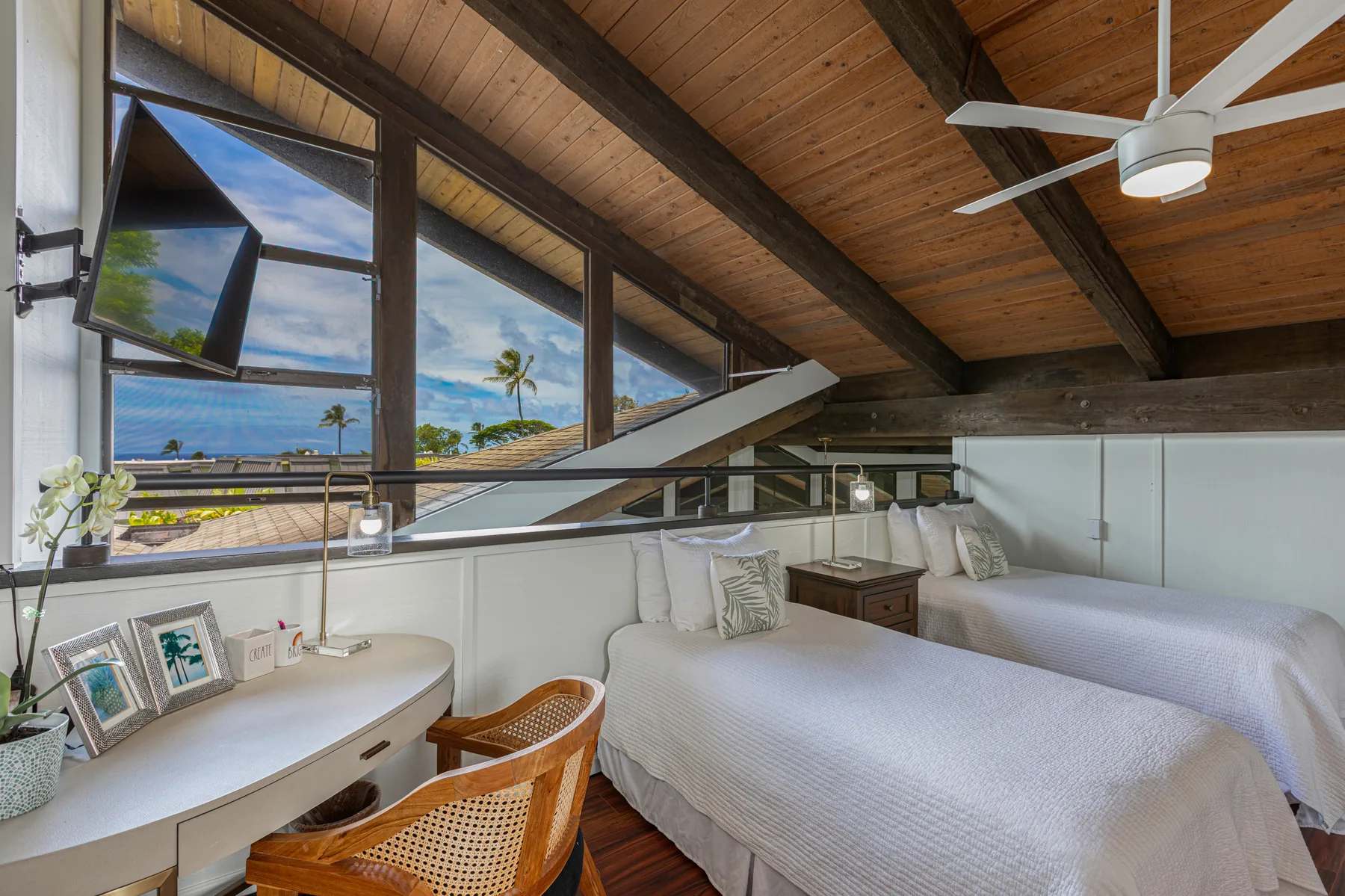 A bright bedroom with two beds beneath a sloped wood ceiling and ocean views.