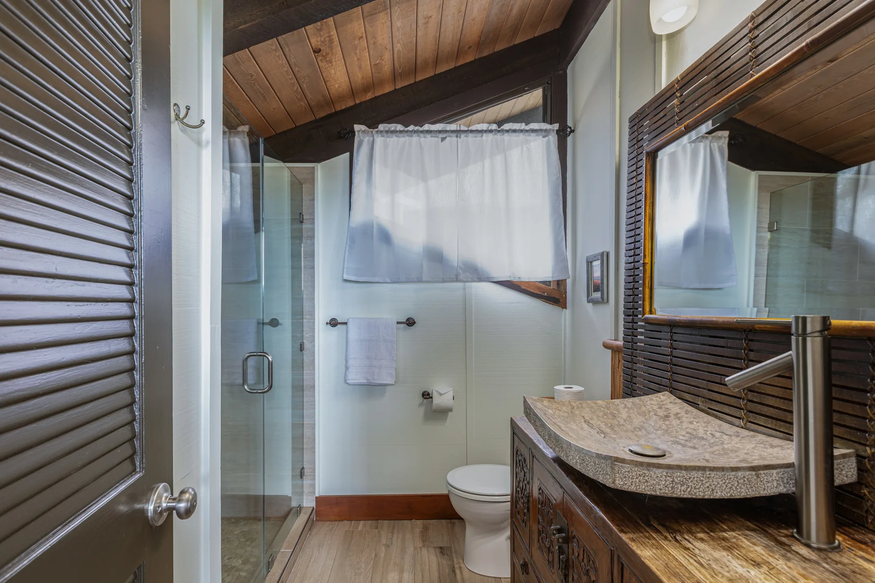 A bathroom with a glass shower, toilet, and wood vanity.