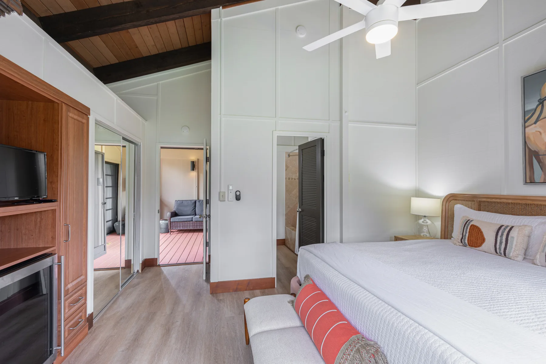 A bright bedroom with a large bed, ceiling fan, and open doorways.