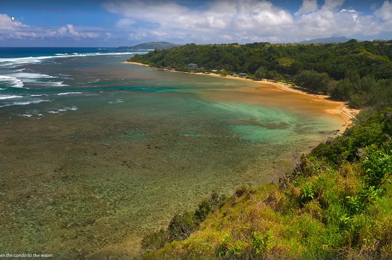 Aerial view of a turquoise bay, sandy shoreline, and forested hills.