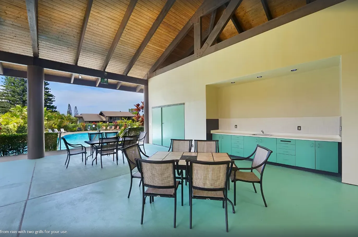 A covered outdoor dining area with tables and seating beside a pool.
