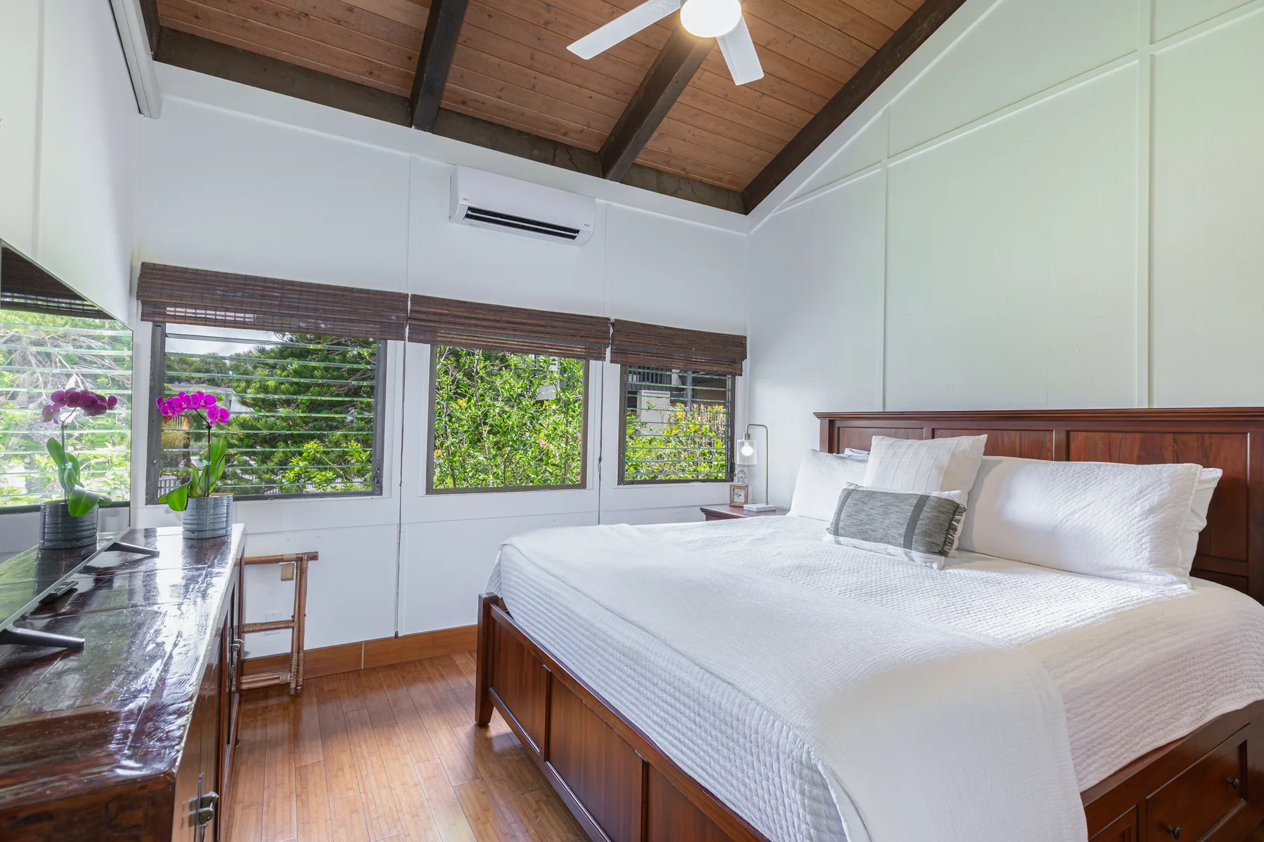 A bright bedroom has a large bed beneath a wood-paneled ceiling.